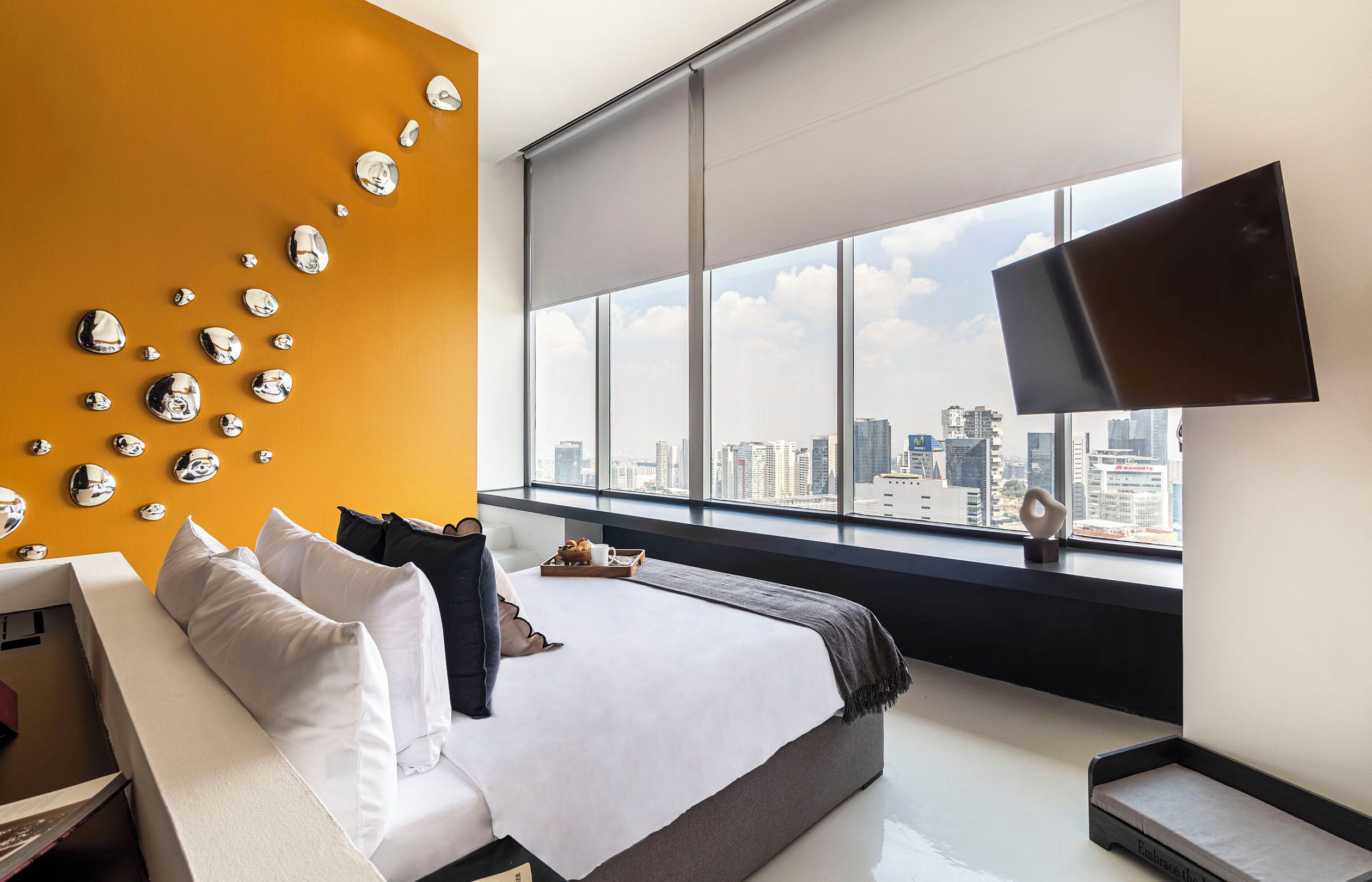 A modern hotel room with a large bed, a city view, and a wall with reflective spherical decorations.