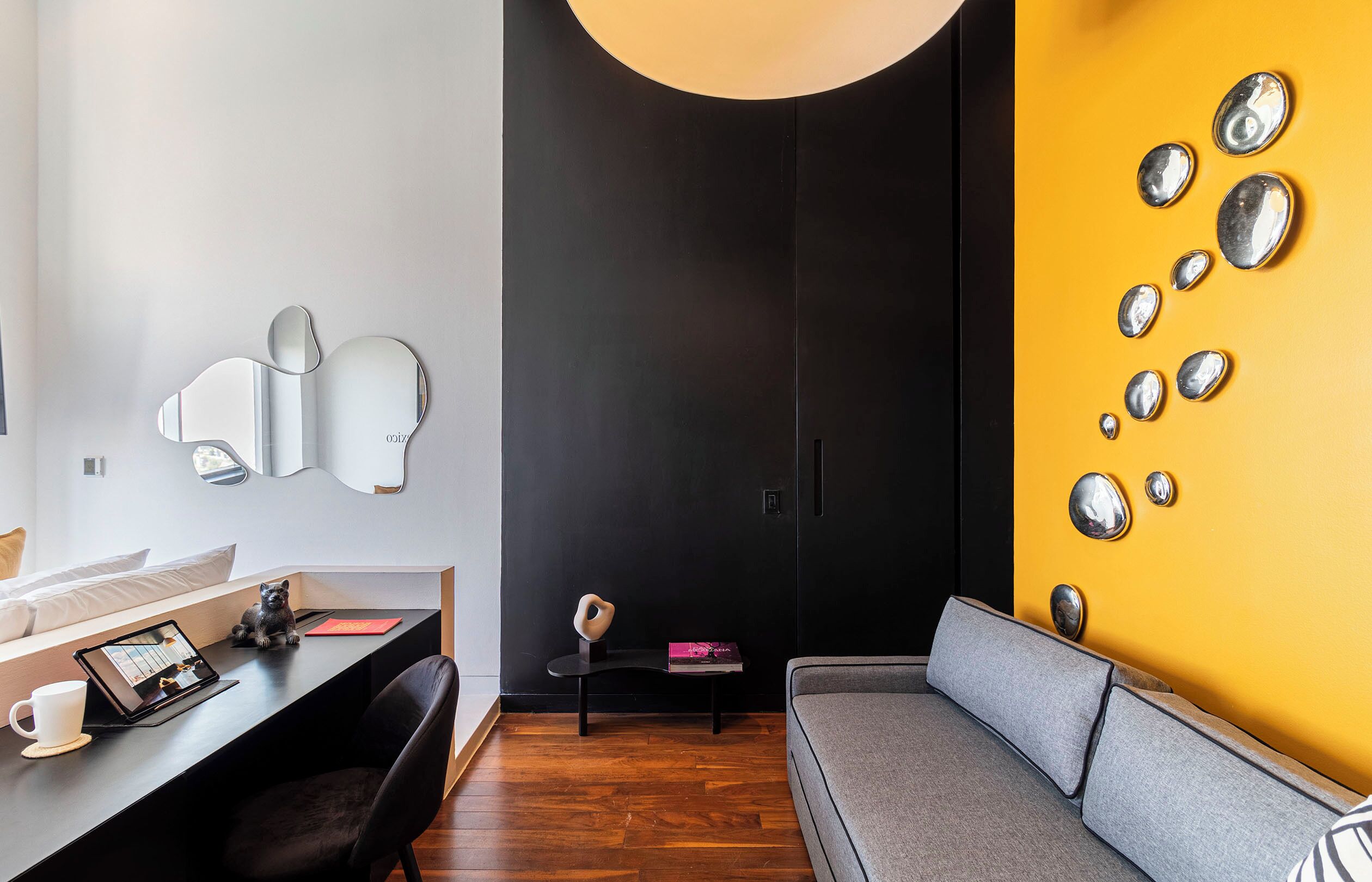 Una habitación moderna con piso de madera, un sofá gris, un escritorio negro con una tableta, una taza blanca y una pequeña figurita de perro.