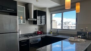 Une cuisine moderne dotée d’appareils électroménagers en acier inoxydable, d’un plan de travail en granit et d’une grande fenêtre offrant une vue sur la ville.