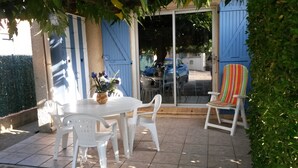 Un patio al aire libre con una mesa, sillas, una verja azul y una planta en maceta.