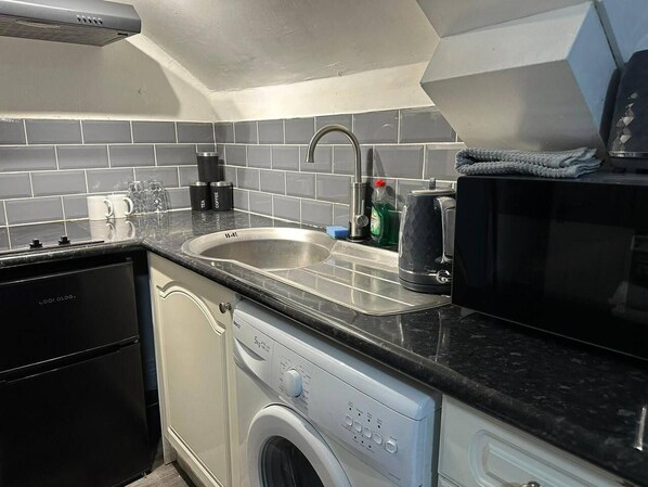 A compact kitchen with a sink, coffee maker, and a washing machine.
