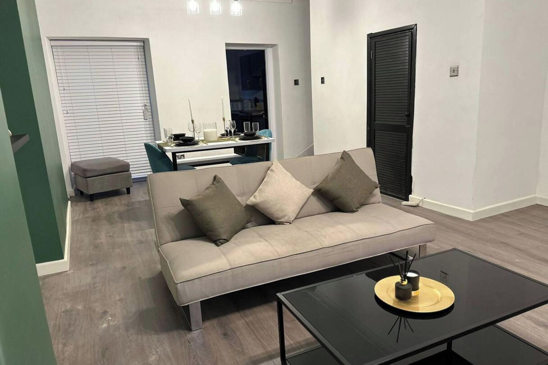 A modern living room with a beige sofa, a glass coffee table, and a dining area in the background.