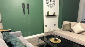 Ein modernes Wohnzimmer mit grüner Akzentwand, einer runden Wanduhr und einem schlichten Couchtisch.