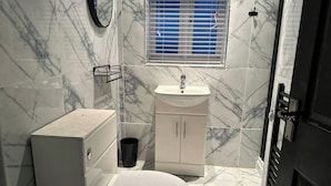 Ein kleines Badezimmer mit Toilette, Waschbecken und Schrank, ausgestattet mit Marmorfliesen und einem Fenster mit Rollo.