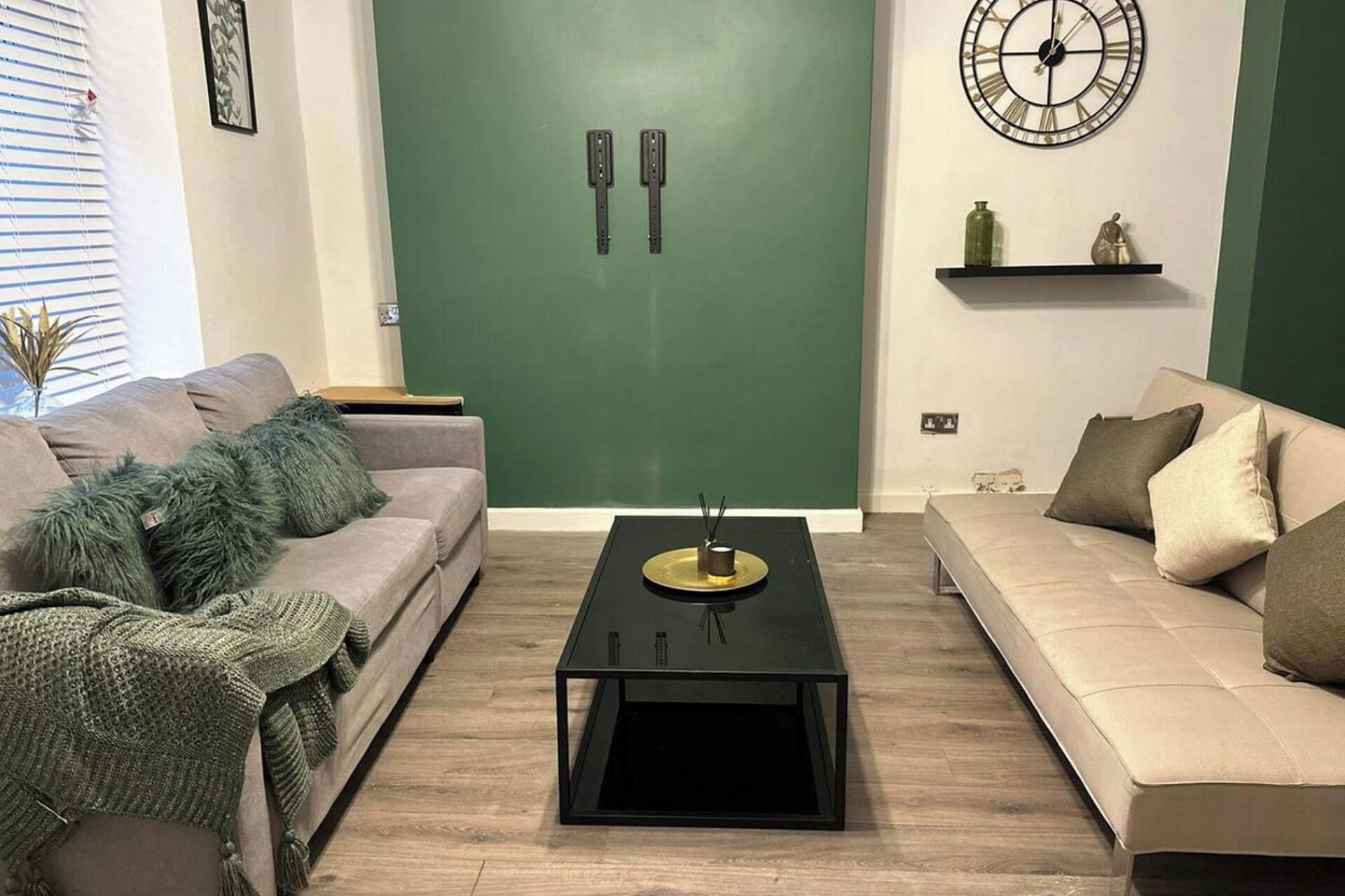 Una sala de estar con dos sofás, una mesa de centro y una pared verde decorativa.