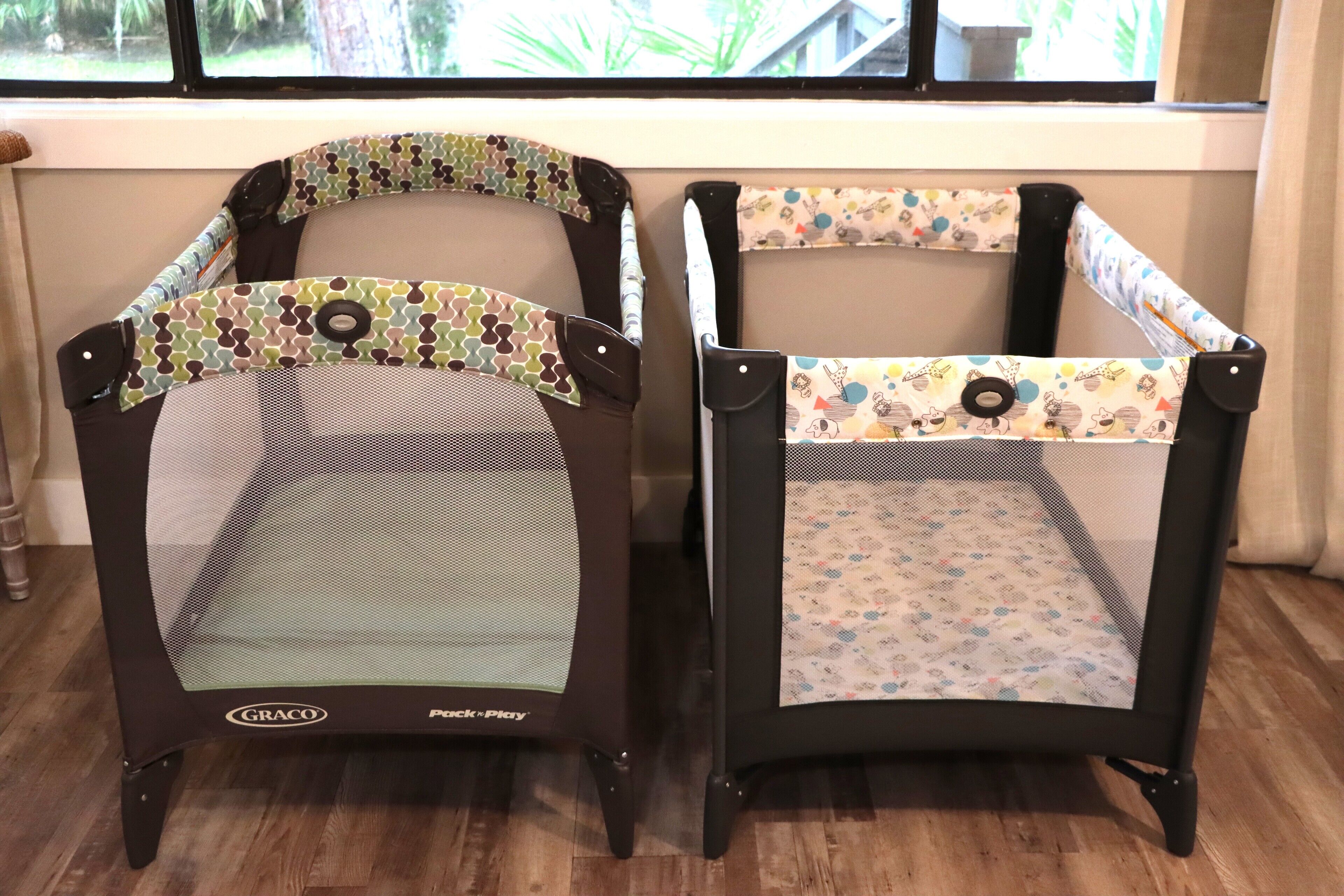Dos cunas Graco Pack-n-Play con laterales de malla, ubicadas en una habitación con suelo de madera y una ventana al fondo.
