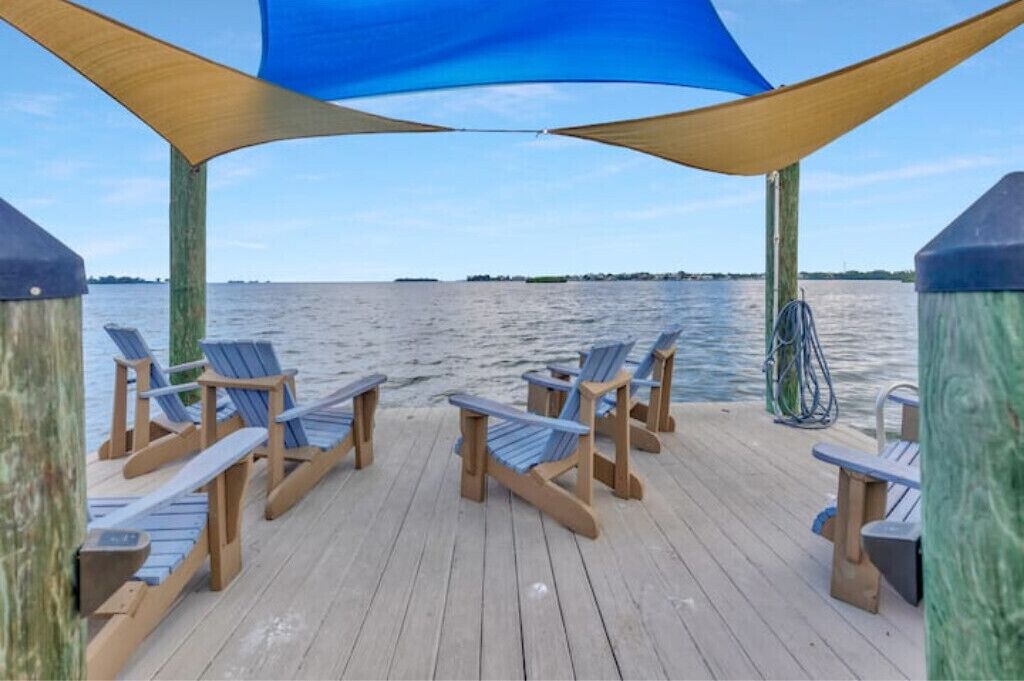 A wooden deck with blue Adirondack chairs and a blue canopy.