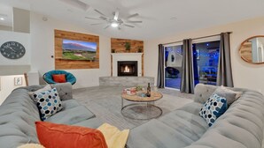 Ein modernes Wohnzimmer mit Kamin, einer Sofagarnitur, einem Couchtisch und einem großen Fenster mit Vorhängen.