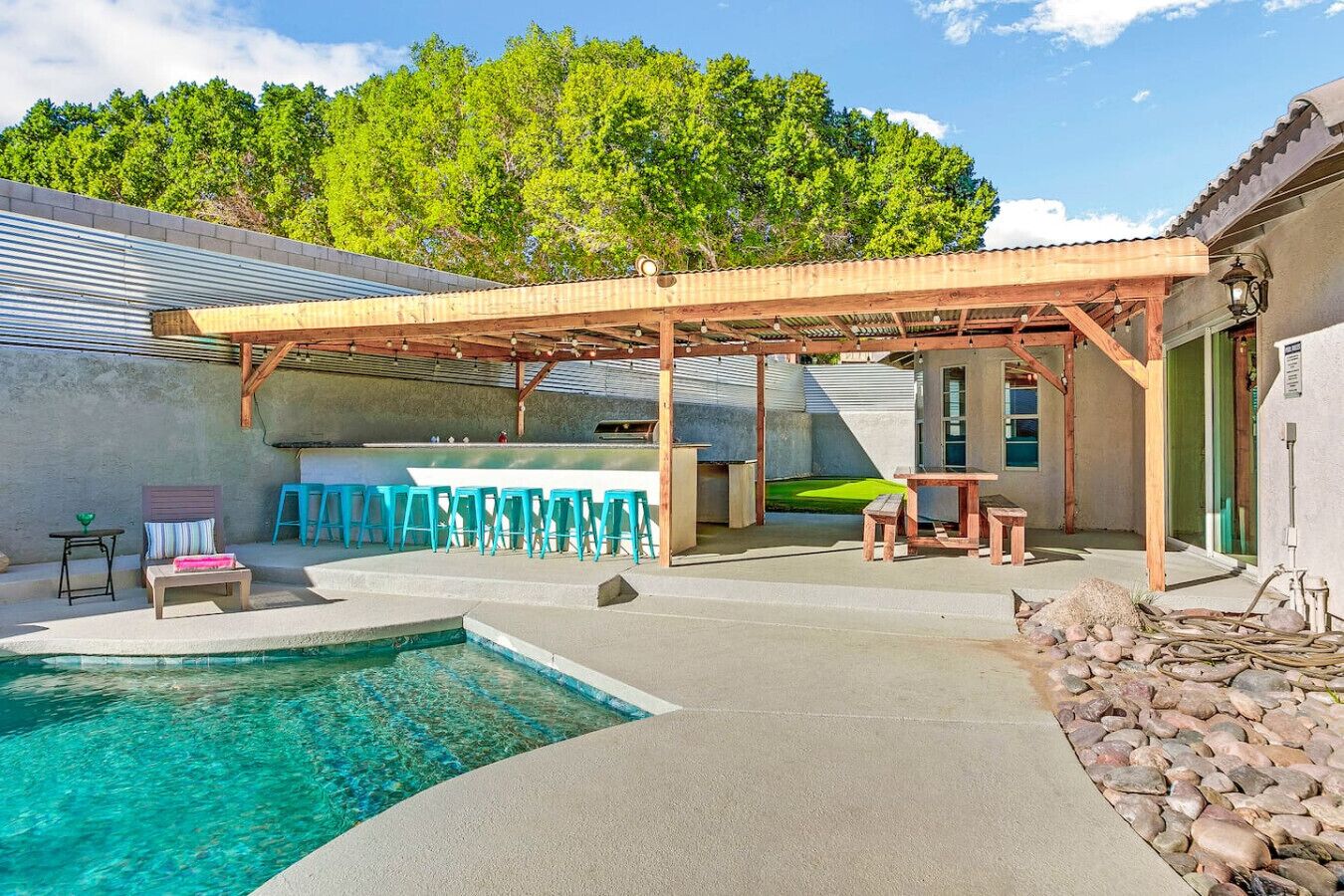 Un giardino con piscina, area salotto all'aperto e una pergola.