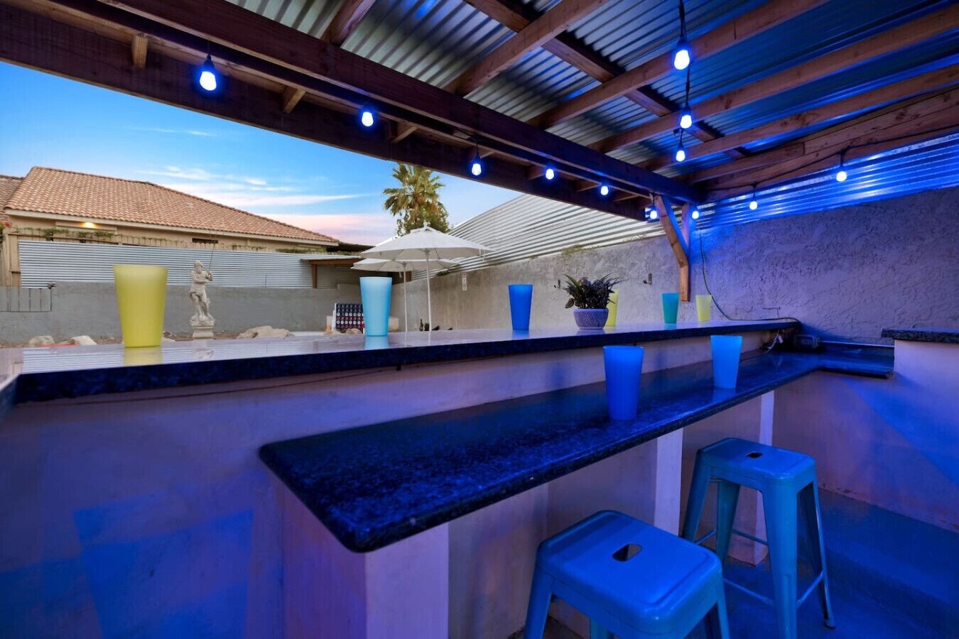 An outdoor bar area with a pool, blue stools, and a statue.