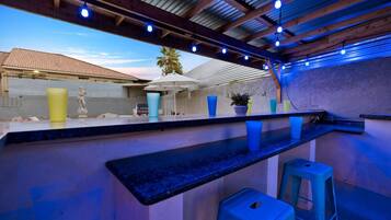 An outdoor bar area with a pool, blue stools, and a statue.
