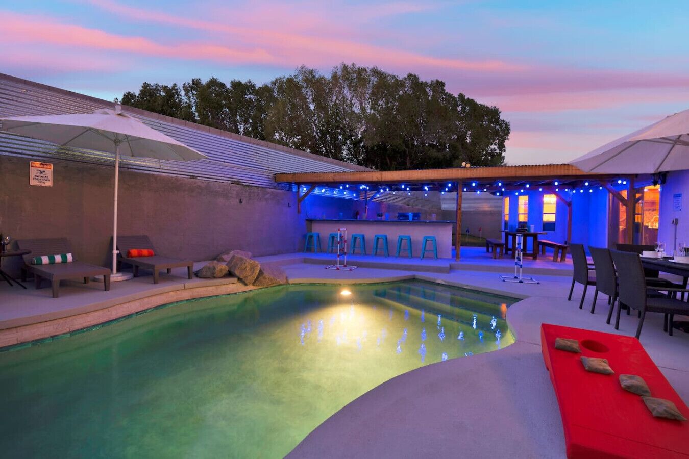 A swimming pool with lounge chairs and a bar area, surrounded by umbrellas and string lights.