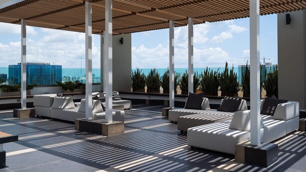 En tagterrasse med hvide sofaer og en træpergola med udsigt over bybilledet.