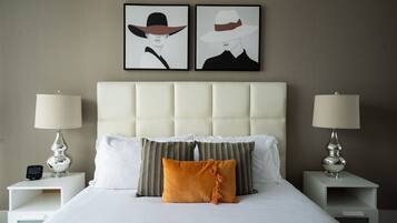 Una cama bien hecha con almohadas blancas y estampadas, dos mesitas de noche con lámparas y dos obras de arte enmarcadas en la pared.