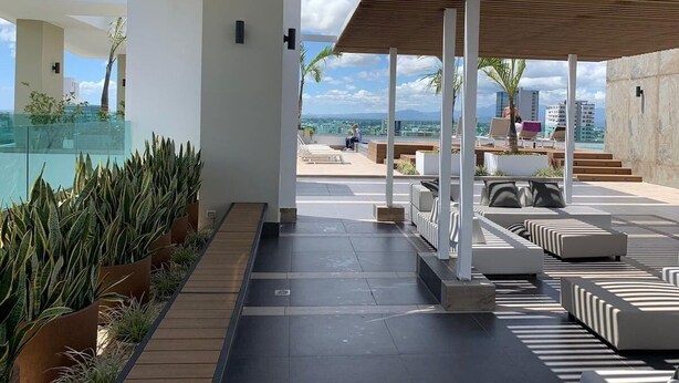 A modern outdoor lounge area with seating and planters, overlooking a cityscape.