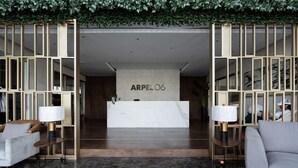 A modern lobby with a reception desk labeled "ARPEL 06," featuring a marble reception counter, a sofa, two lamps, and a patterned rug.