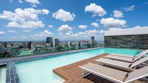 A rooftop infinity pool with lounge chairs, a city view, and a stone wall.