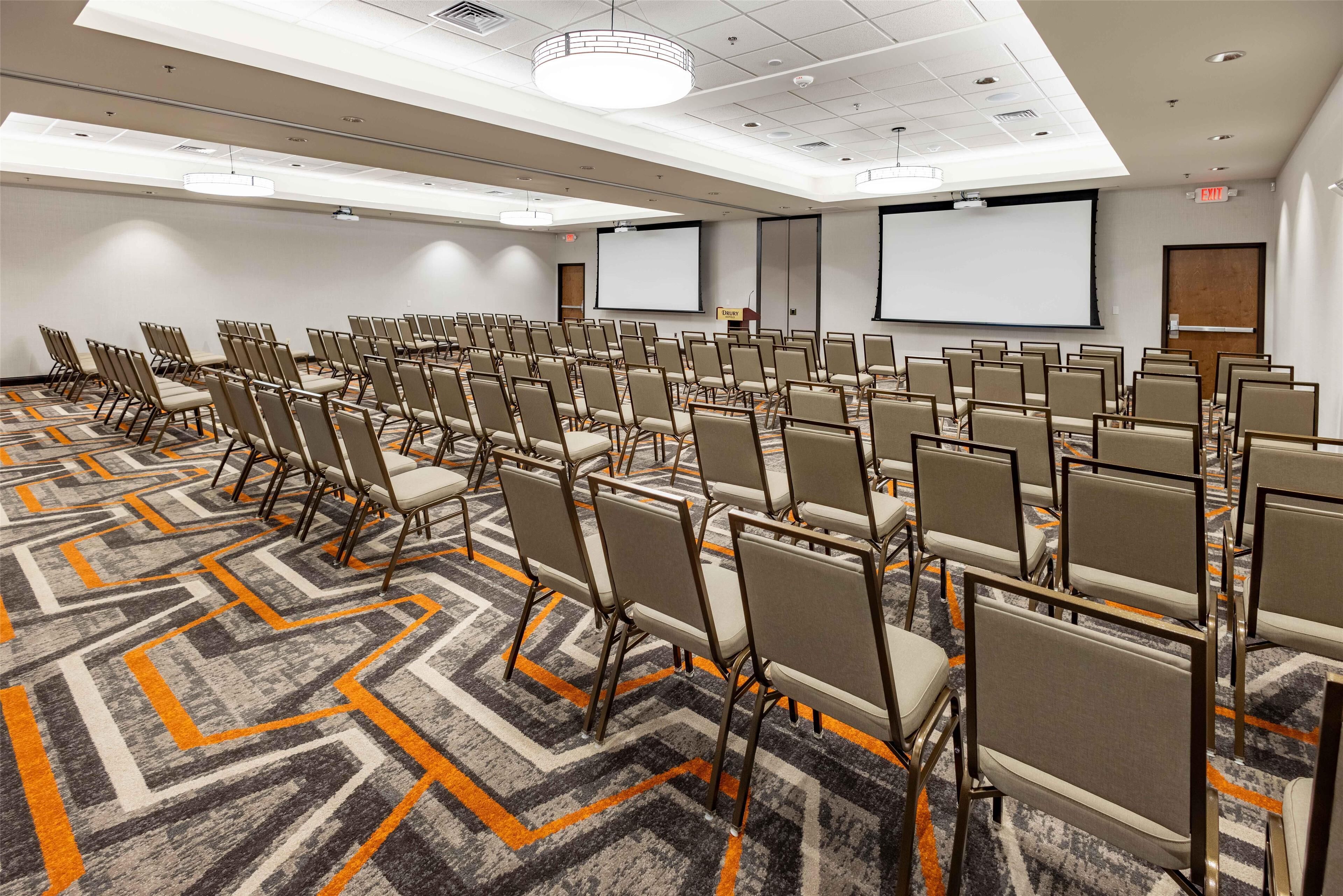A conference room with rows of chairs, a projector screen, and a carpeted floor.
