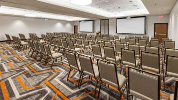 A conference room with rows of chairs, a projector screen, and a carpeted floor.