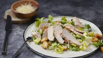 Une assiette de viande tranchée, accompagnée de croûtons et de laitue, posée sur une surface sombre.