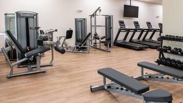 Ett gym med olika typer av träningsutrustning, inklusive löpband, styrketräningsmaskiner och hantlar.