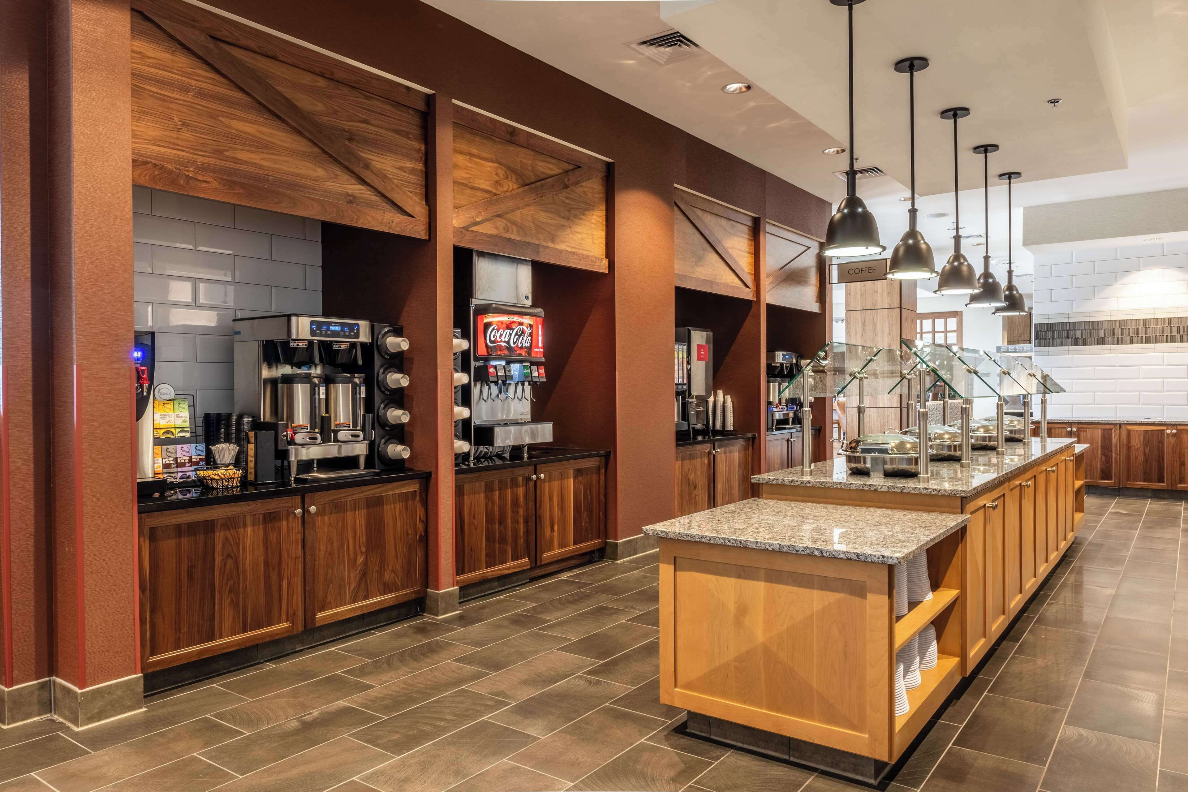 A modern kitchen area with wooden cabinets, a coffee station, and a glass display case.