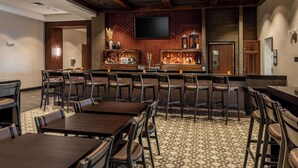 A bar area with multiple seating options, a television mounted on the wall, and a variety of bottles on shelves. - Drury Plaza Hotel Dallas Arlington (Arlington)