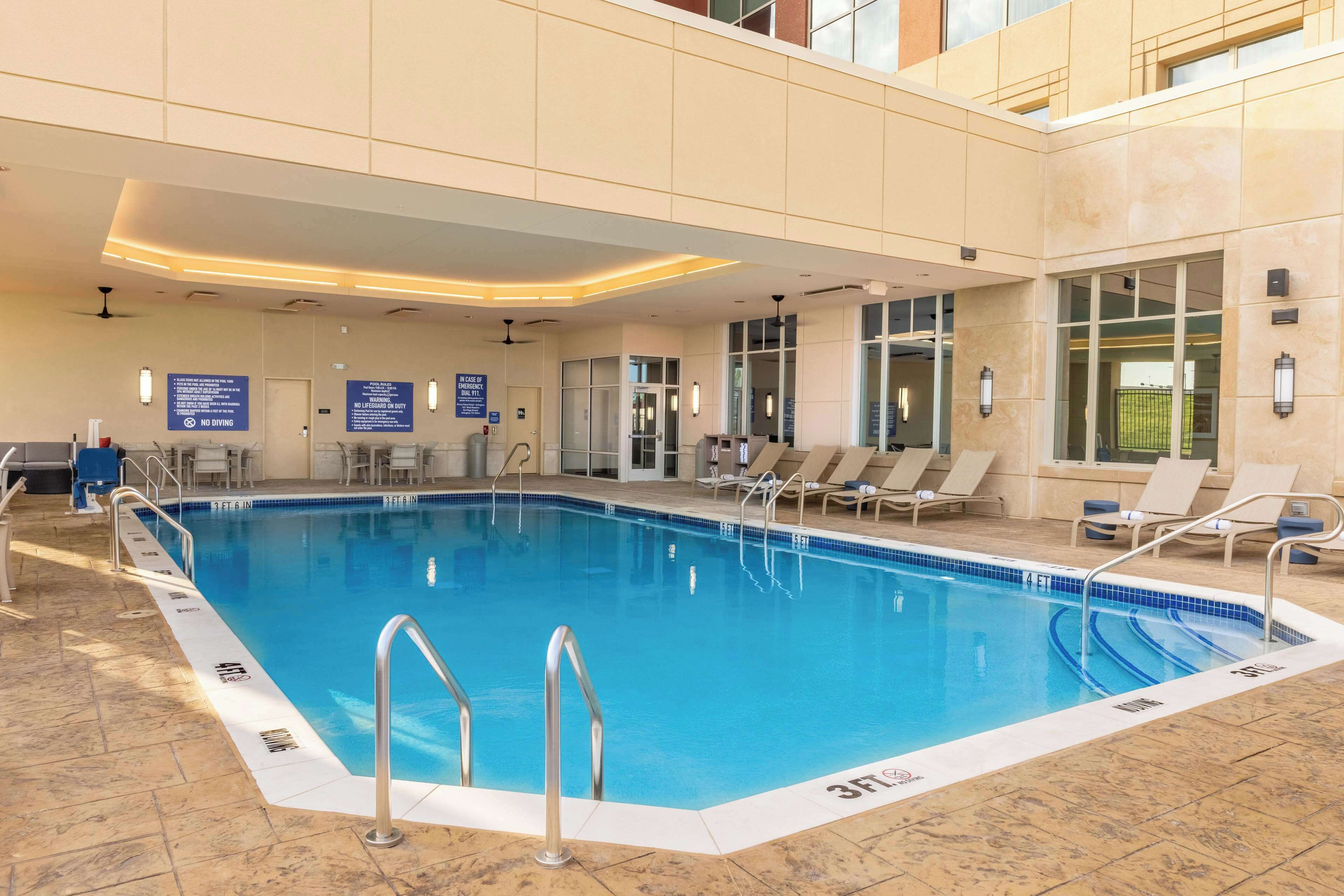 Una piscina interior con zonas despejadas alrededor, sillones reclinables y señalización informativa.