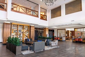 Un hall d’entrée spacieux avec un plafond haut, des éléments décoratifs en bois et un espace détente comprenant des canapés et des fauteuils.