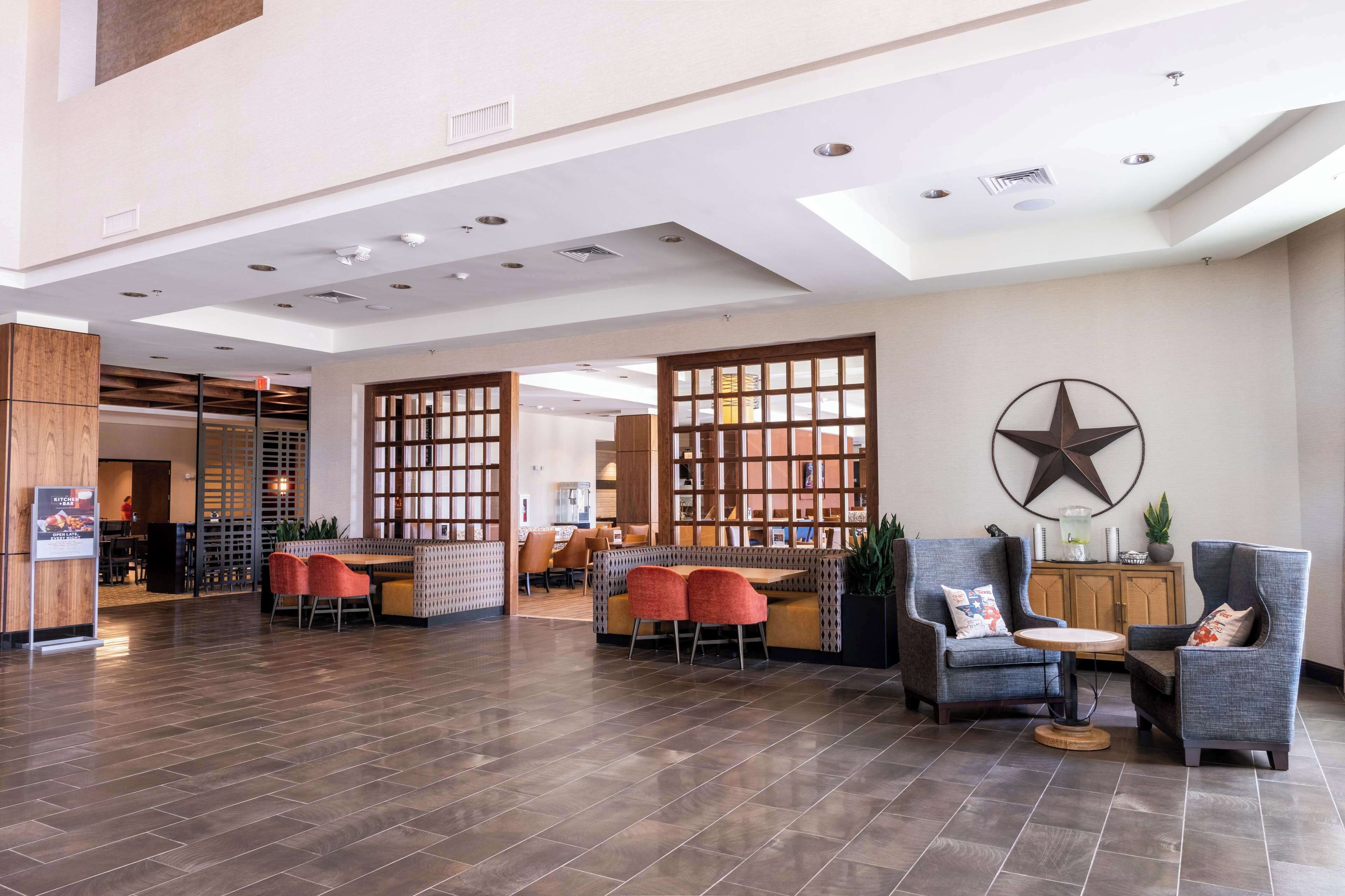 A spacious lobby with a high ceiling, recessed lighting, and a large star decoration on the wall. There are seating areas with modern chairs and a small round table.