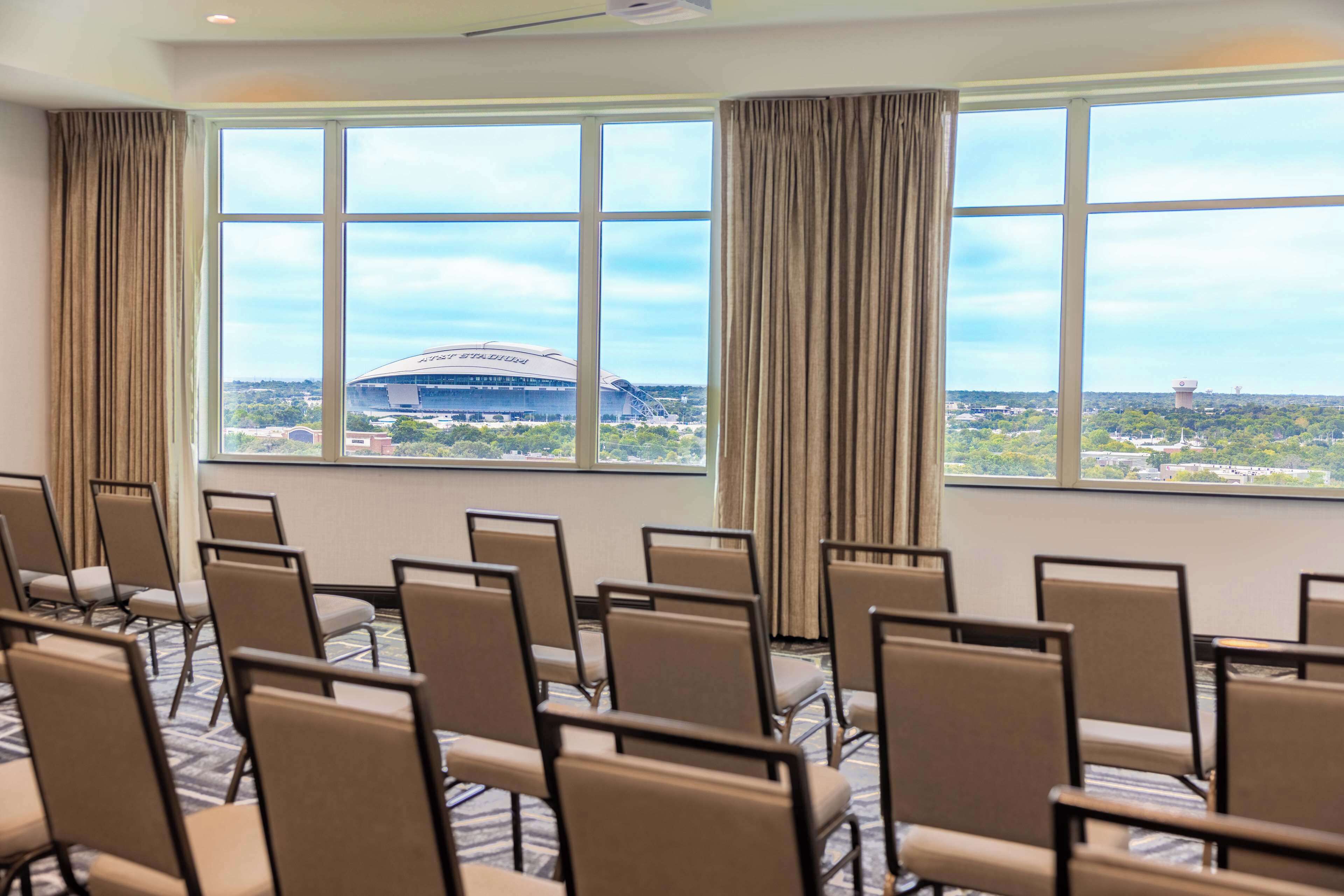 A conference room with rows of chairs and large windows offering a view of a stadium and surrounding area.