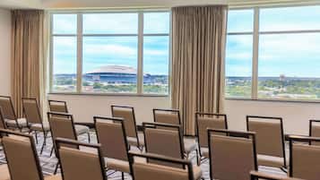 A conference room with rows of chairs and large windows offering a view of a stadium and surrounding area.
