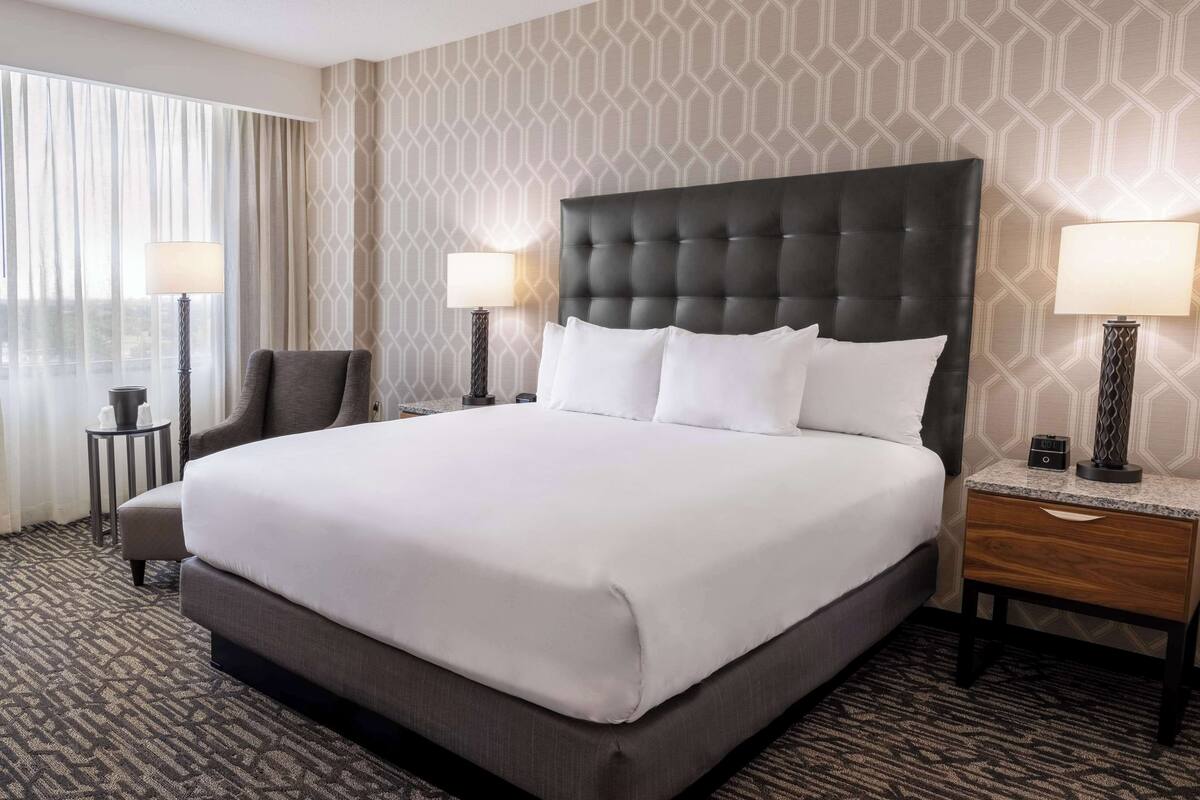 Ein Hotelzimmer mit einem großen Bett, zwei Nachttischen mit Lampen, einem Sessel und einem gemusterten Teppich.