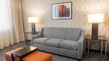 A hotel room with a patterned sofa, two side tables with lamps, a framed picture on the wall, and a patterned carpet.