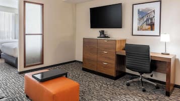 A hotel room with a bed, a desk, a chair, a TV, a framed picture, and a large window.