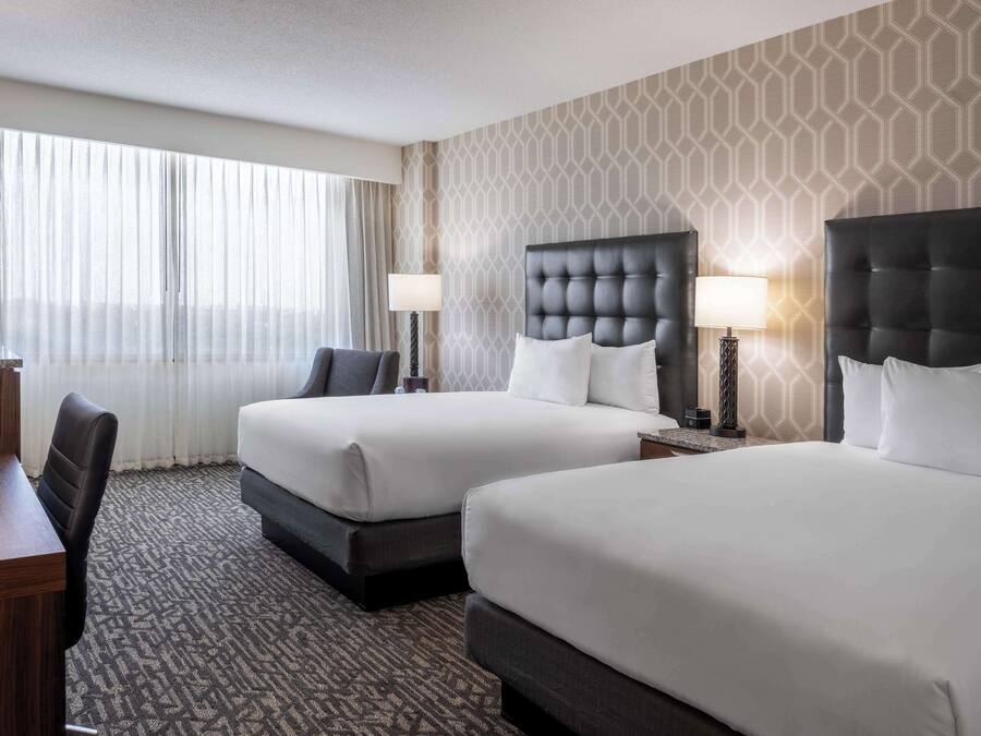 A hotel room with two beds, a desk, and a chair.