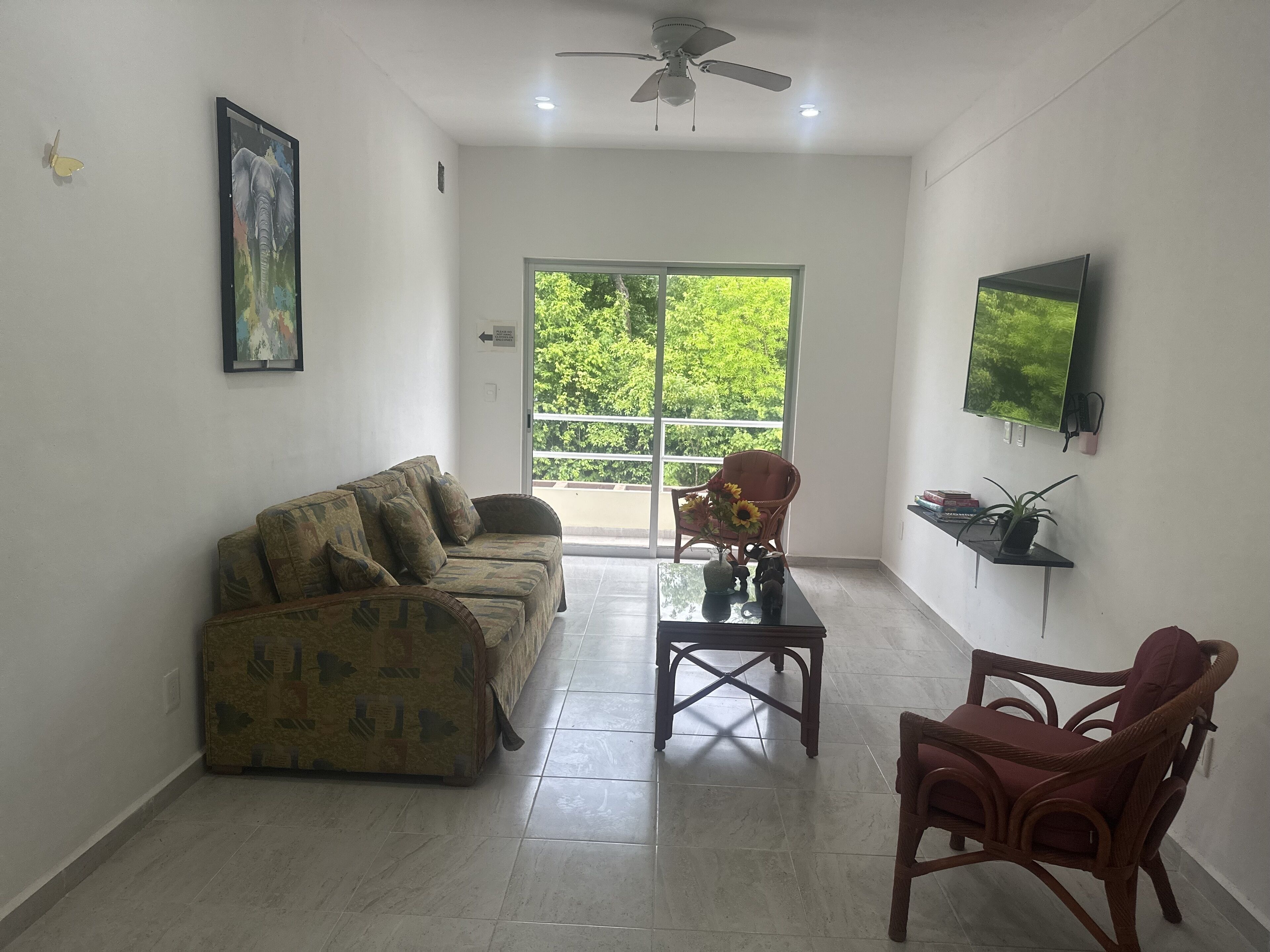 A spacious living room with a sofa, armchairs, a coffee table, and a TV mounted on the wall.