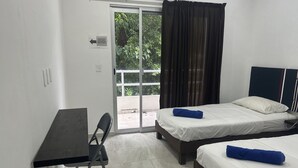 A hotel room with a desk, two beds, and a view of greenery through a sliding door. - Cozy Apartment 1B Puerto Morelos  (PUERTO MORELOS)