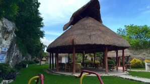 A thatched-roof gazebo with a dining area and outdoor seating. - Cozy Apartment 1B Puerto Morelos  (PUERTO MORELOS)