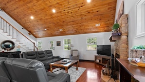 Amplia sala de estar con techo de madera alto, chimenea, sofás de cuero y televisor.