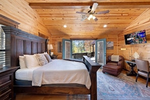 Quarto de cabana de madeira com uma cama grande, um ventilador de teto, televisão e vista para o exterior.