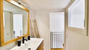 Een badkamer met een witte wastafel, een spiegel met houten lijst en een raam.
