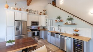 Une cuisine moderne avec des meubles blancs, des appareils en acier inoxydable et une table à manger en bois.