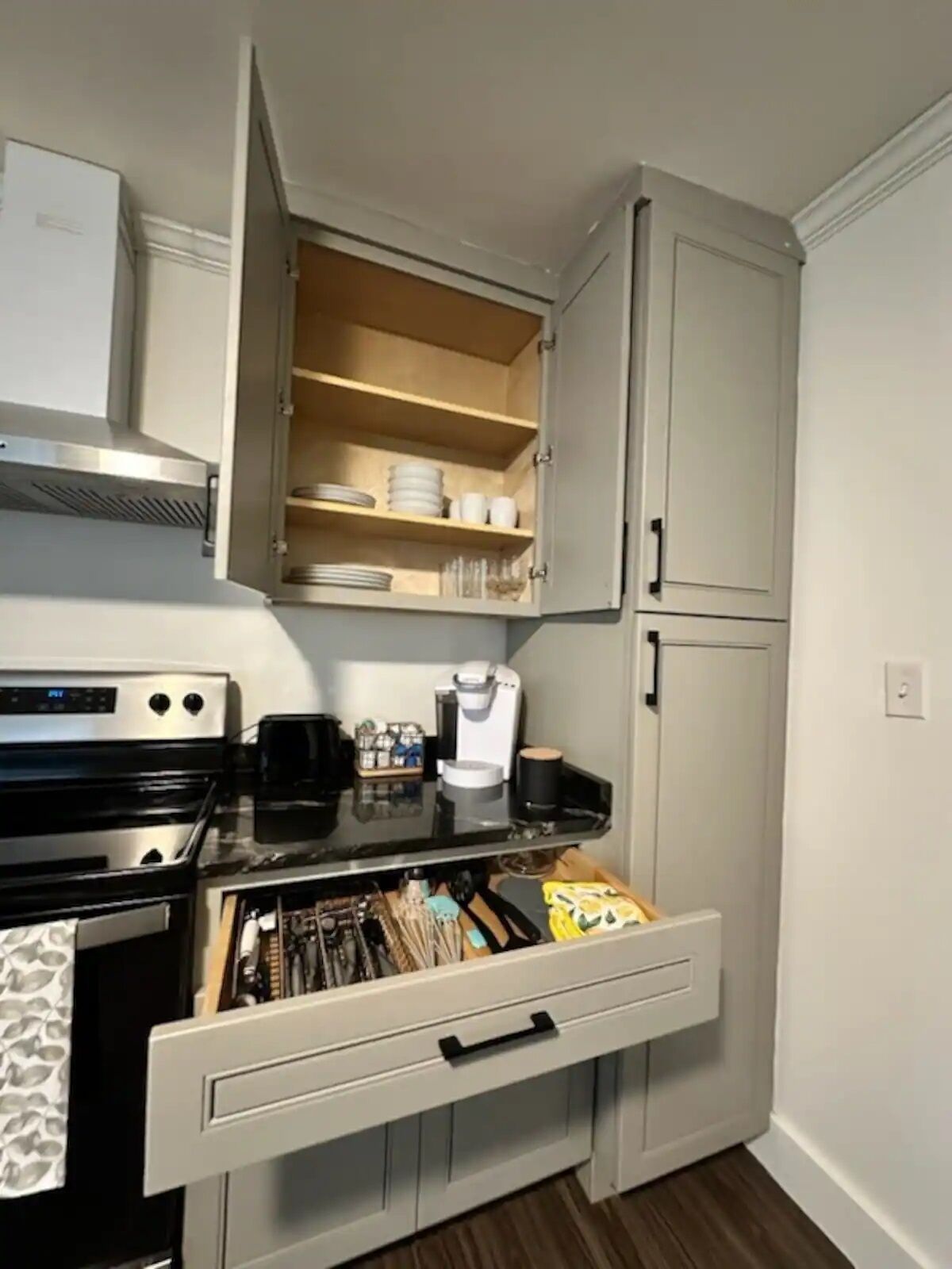 Eine kompakte Küche mit Einbauofen, Kaffeemaschine und einem Schrank mit Einlegeböden.