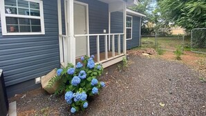 Una casa con porche cubierto, camino de grava y un arbusto de hortensia azul.