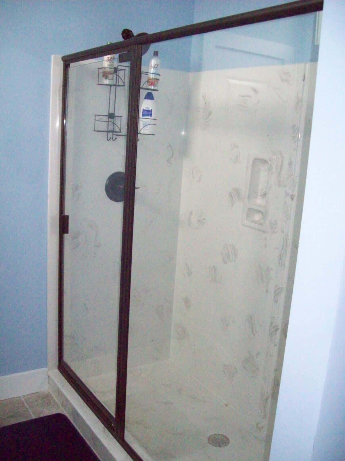 A glass-enclosed shower with a white tiled wall and a small shelf with toiletries.