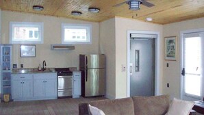 Een keuken met een koelkast, oven en spoelbak. Er is een plafondventilator en een deur naar een andere kamer.