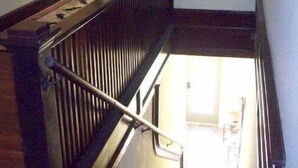 Een houten trap met een leuning die naar een verdieping leidt. Boven de trap is een klein raam met donkere omlijsting te zien.