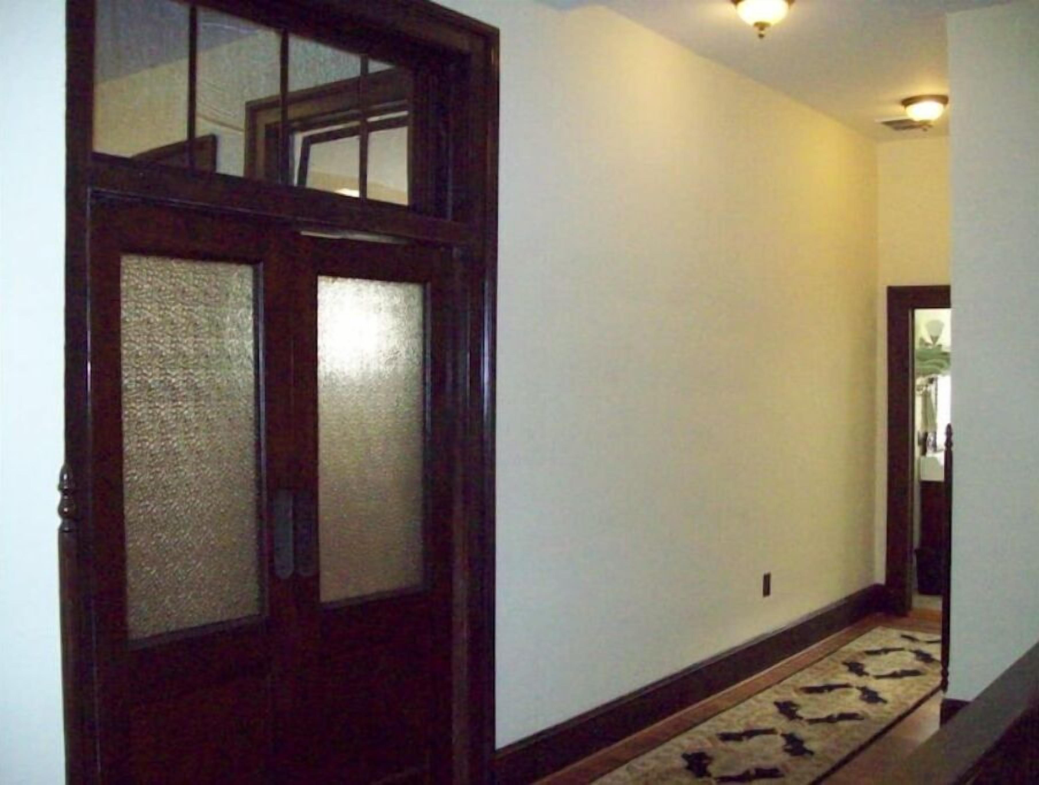 Un couloir avec une porte en bois dotée de panneaux en verre dépoli, un tapis à motifs et un luminaire au plafond.