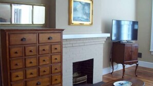 Een woonkamer met een open haard, een televisie, een houten kast en een grote spiegel.